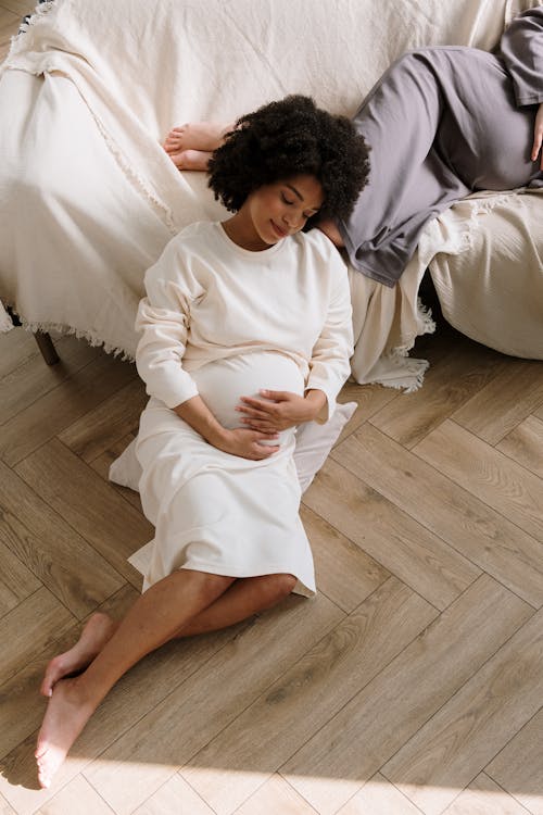 Free Pregnant Woman in White Long Sleeve Dress Sitting on the Floor Stock Photo