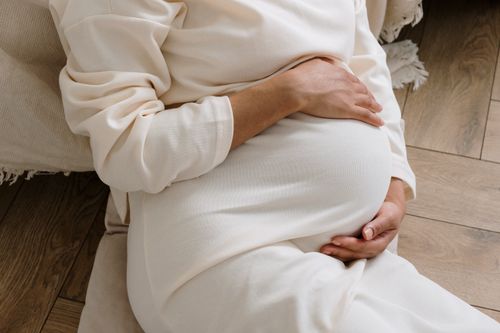 Free A serene moment of a pregnant woman in a cozy white dress holding her belly. Stock Photo