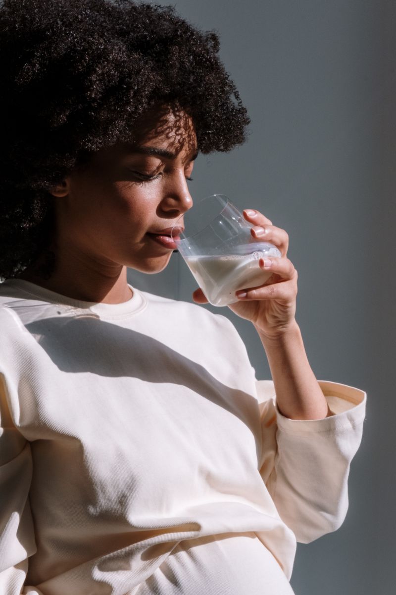 A Black woman drinks a glass of milk in soft daylight. Most Black adults make less lactase after childhood, but many still tolerate small amounts of dairy.