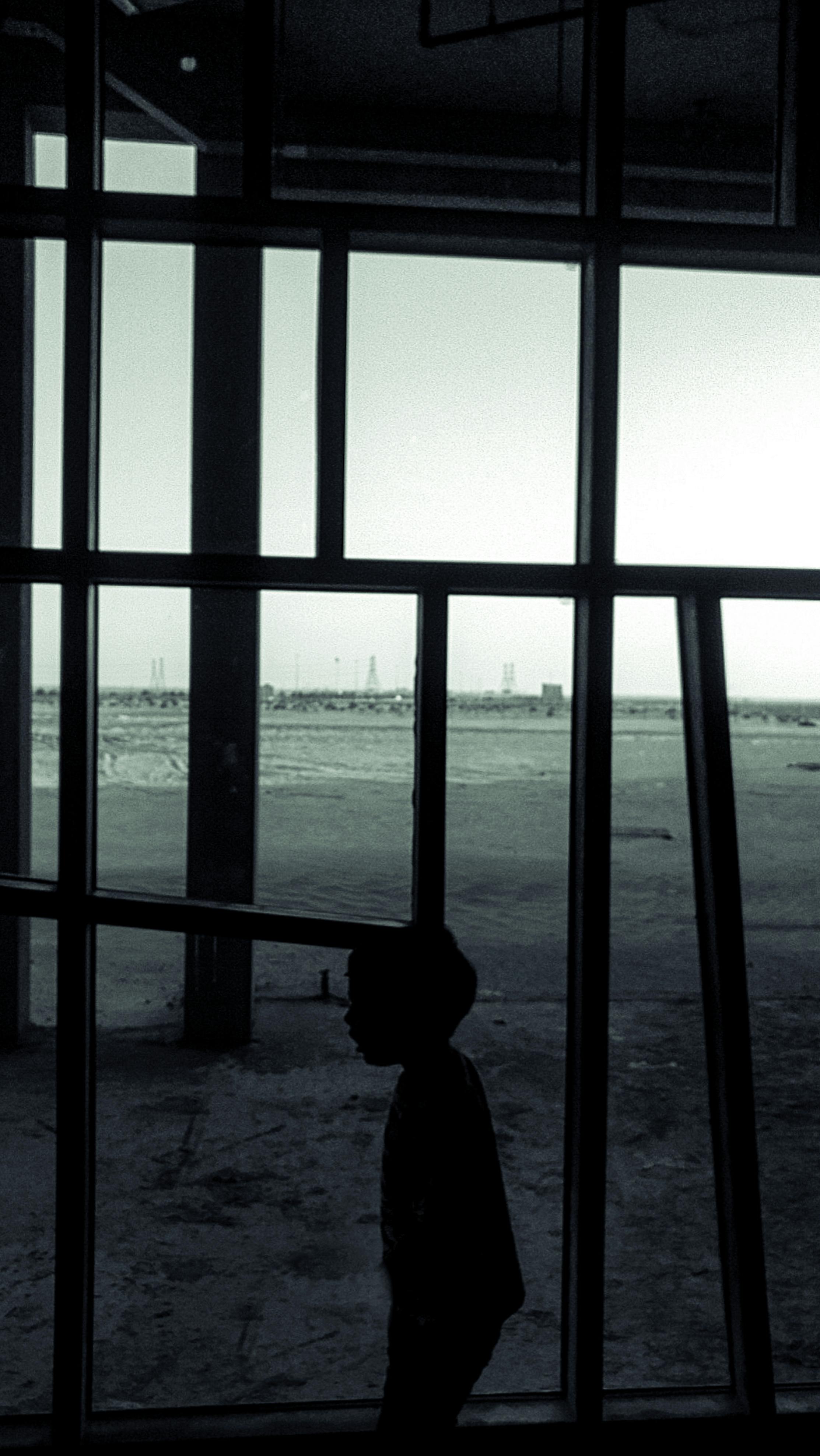 Silhouette of a child seen through window frames in a stark, architectural setting.