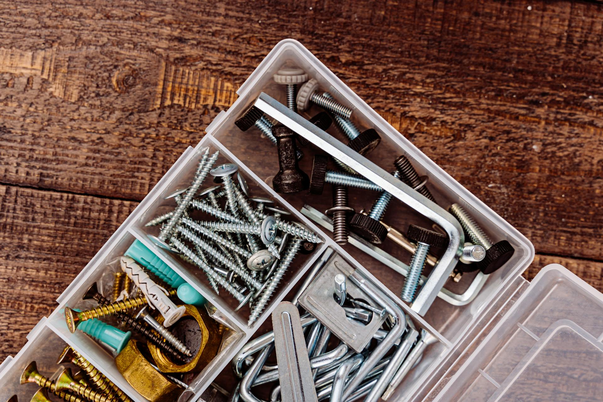 Top view of assorted screws and bolts in a plastic organizer on a wooden surface.