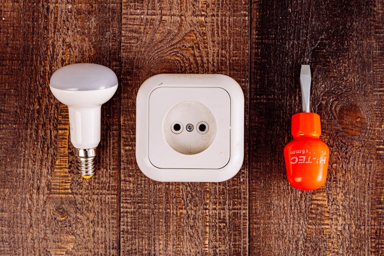 An Outlet Screwdriver And A Lightbulb On A Wooden Surface