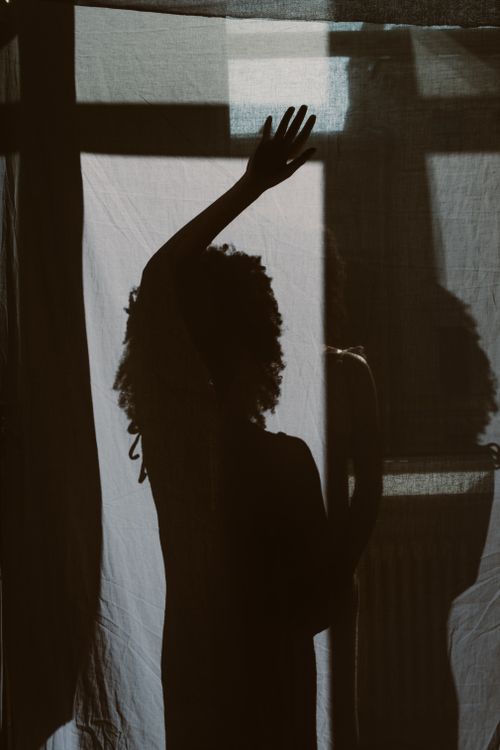 Free Moody silhouette of a woman raising her hand behind a curtain, capturing a play of light and shadow. Stock Photo