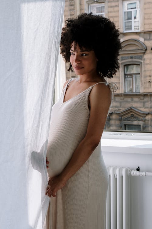 A Pregnant Woman Standing Beside the White Curtain while Looking Afar