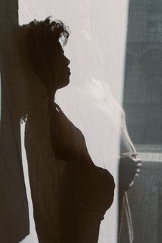 窗帘后，一名孕妇的艺术轮廓凸显了她的肚子