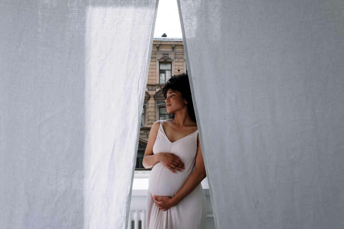 Expecting mother in a white dress holding her baby bump