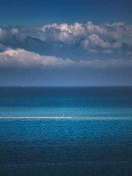 Two people walking along a sandbar in New Zealand under a dramatic cloudy sky.