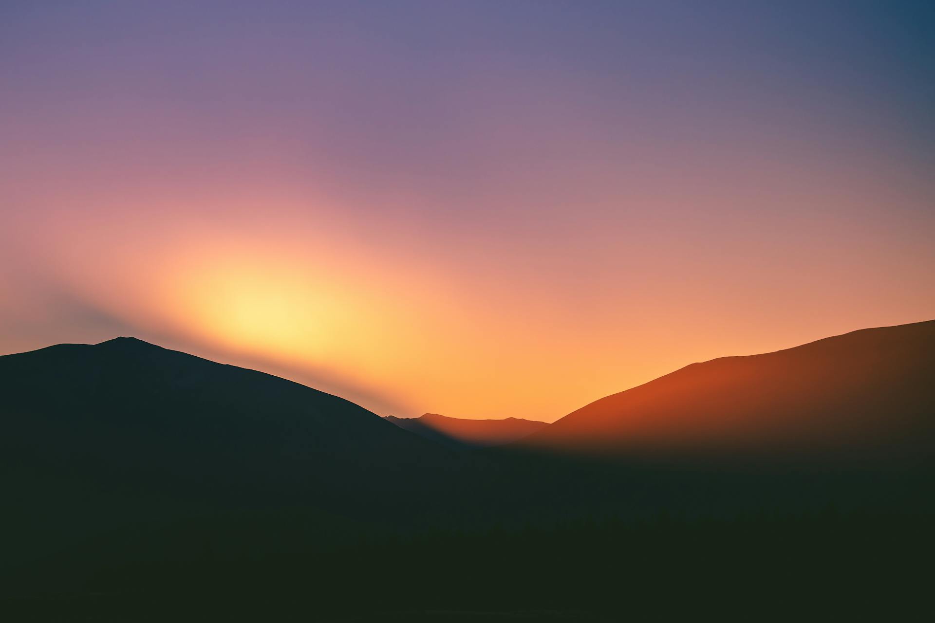 A tranquil sunset over mountains in New Zealand, showcasing a vibrant gradient sky.