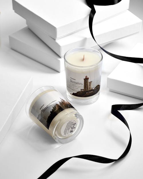 From above of glass jars of scented candles with stickers filled with white wax on table with black ribbon and white boxes