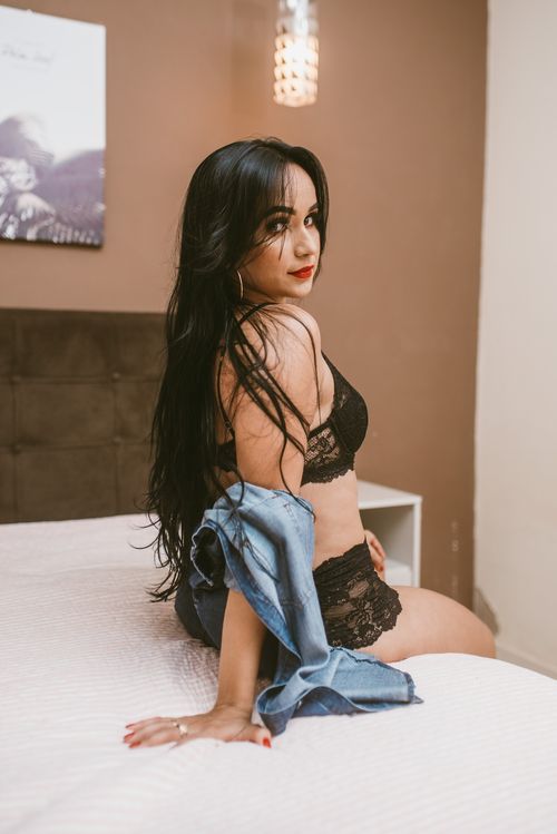 Free A woman in black lingerie sitting on a white bed with a stylish interior setting. Stock Photo