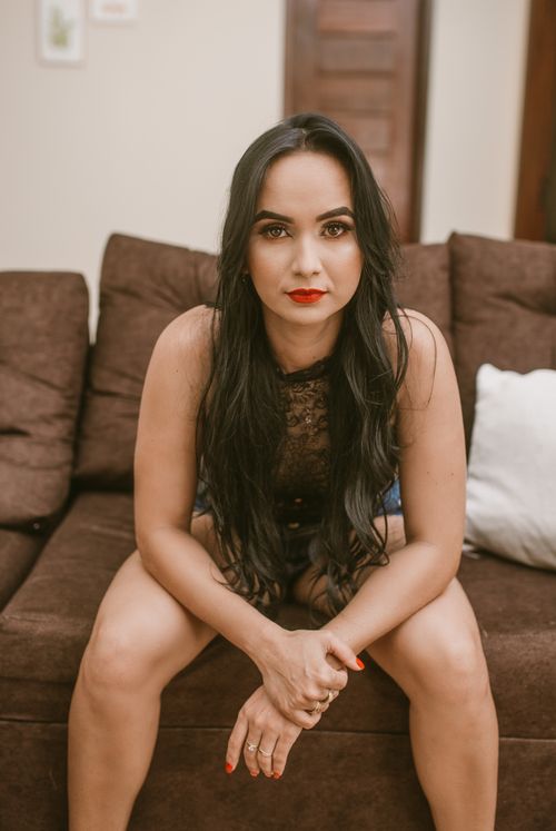 Free Portrait of a woman sitting on a brown couch indoors with a focused expression. Stock Photo