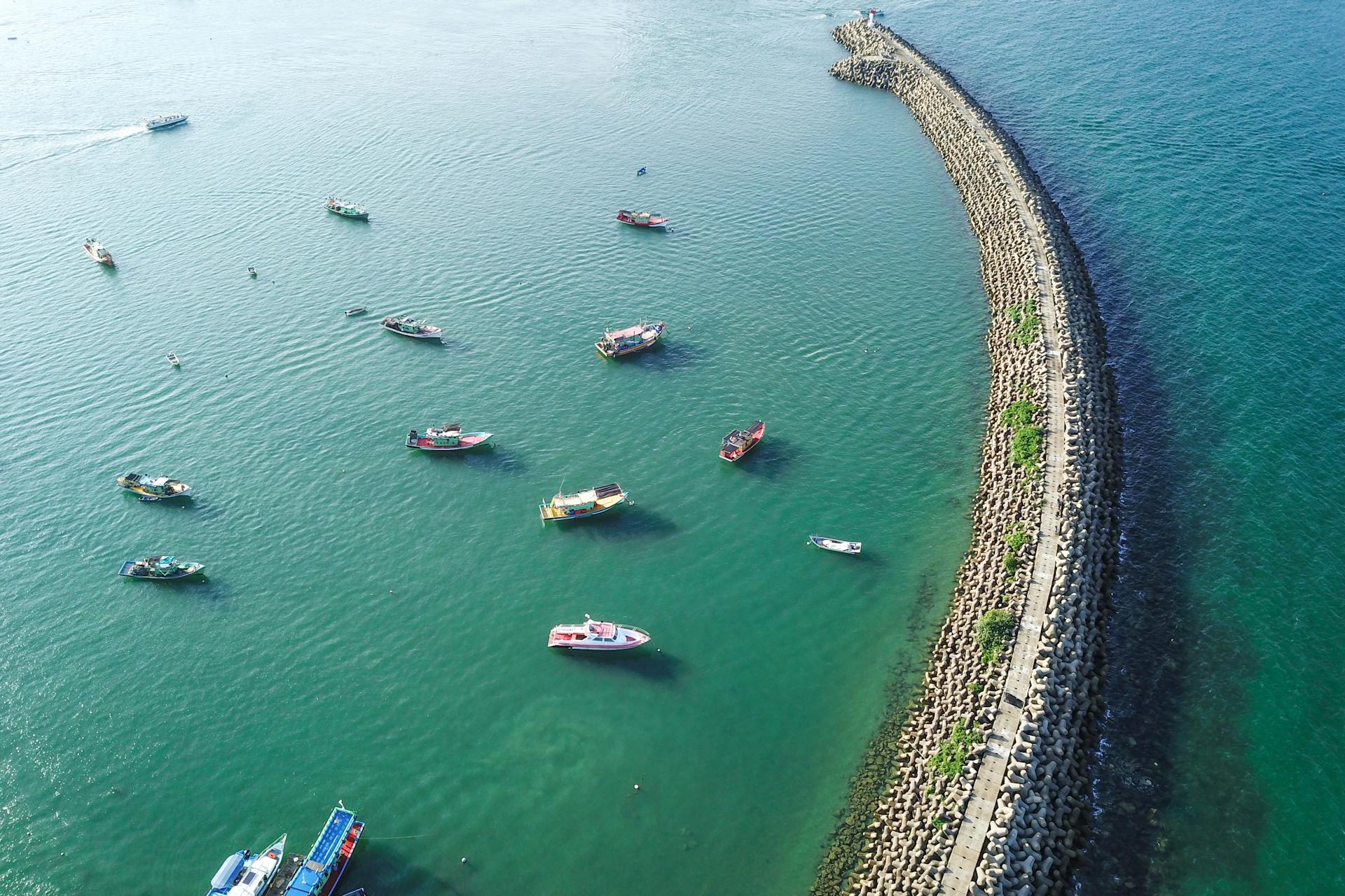Aerial view of turquoise tranquil sea with massive long breakwater construction and many motorboats on clear weather