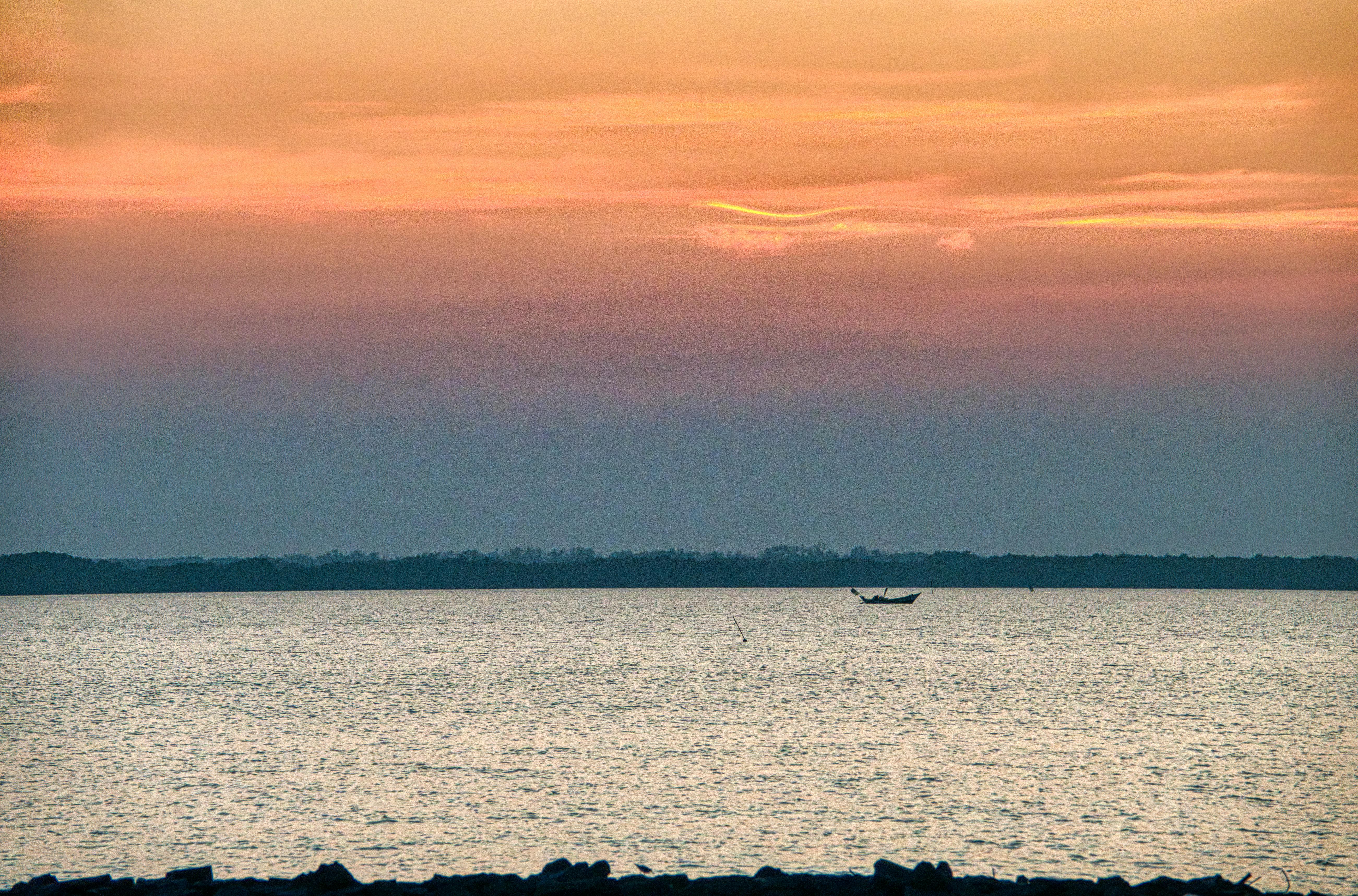 Picturesque view of boat on rippled sea water against tree silhouettes under colorful sky at sundown