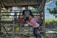 Side view of cheerful little Asian girl in casual clothed smiling and running while spending time with happy father sitting in rustic wooden cabin in village