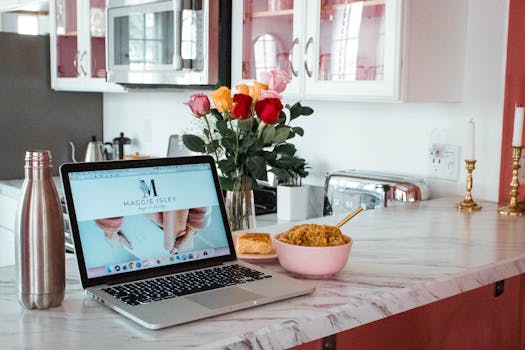 Modern kitchen counter with laptop, snack, and flowers, perfect for a home office setup.
