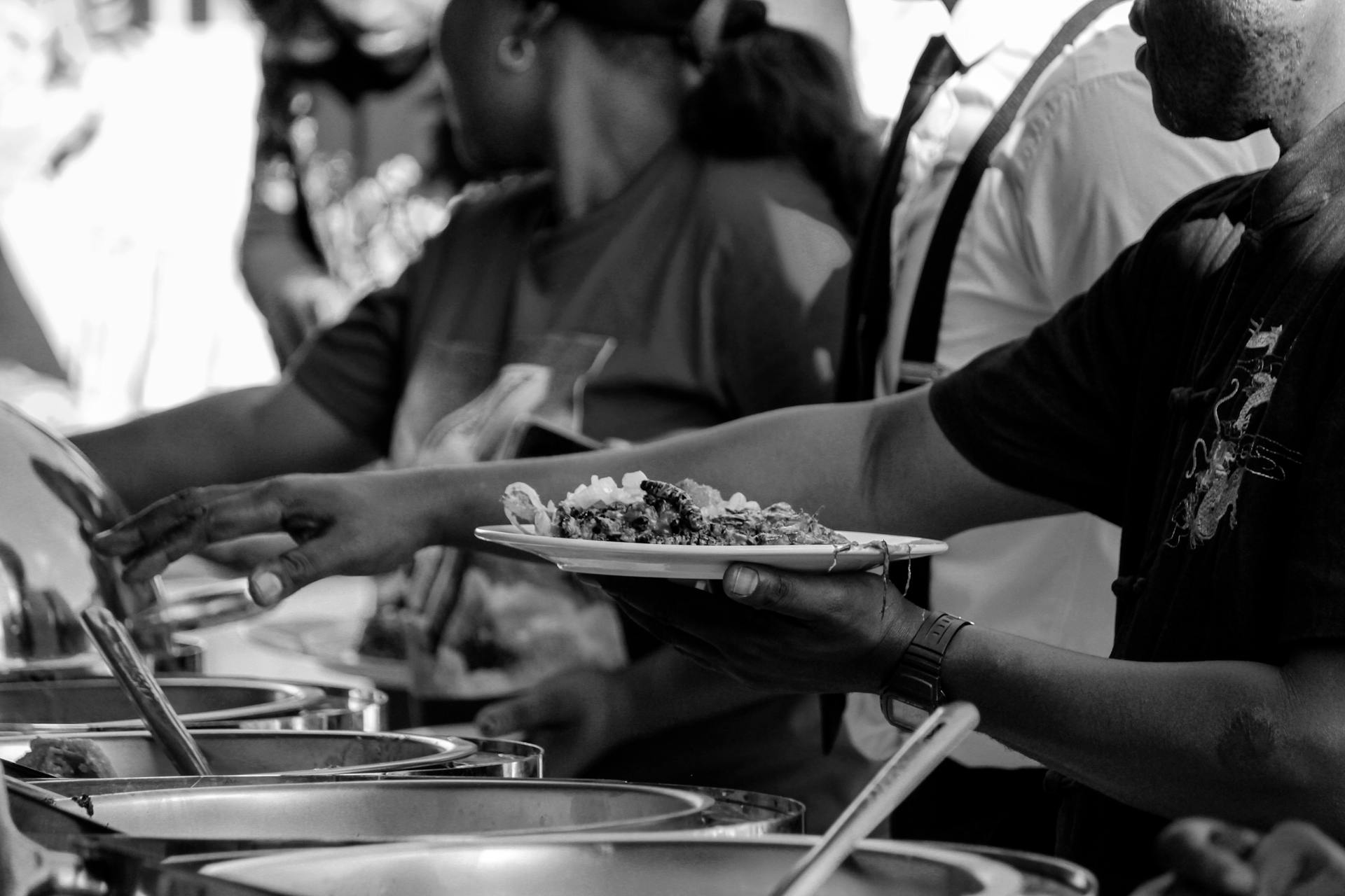 A monochrome image capturing a buffet line at a social event, highlighting diverse people serving food.