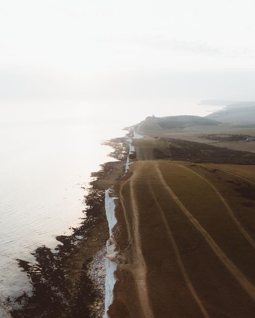 Free Drone view of top of rocky cliff covered with grass located on coast near calw ocean against foggy sky in nature Stock Photo