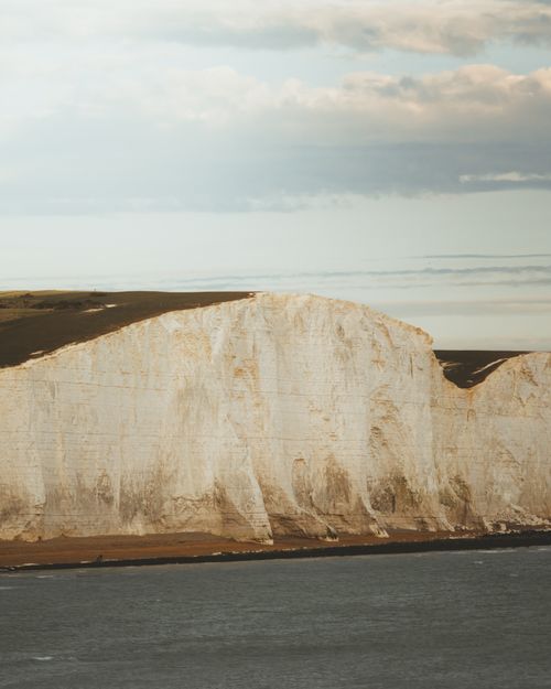 Free Stony formation with grass on top located on rocky coast with calm water against cloudy sky in nature in daylight Stock Photo