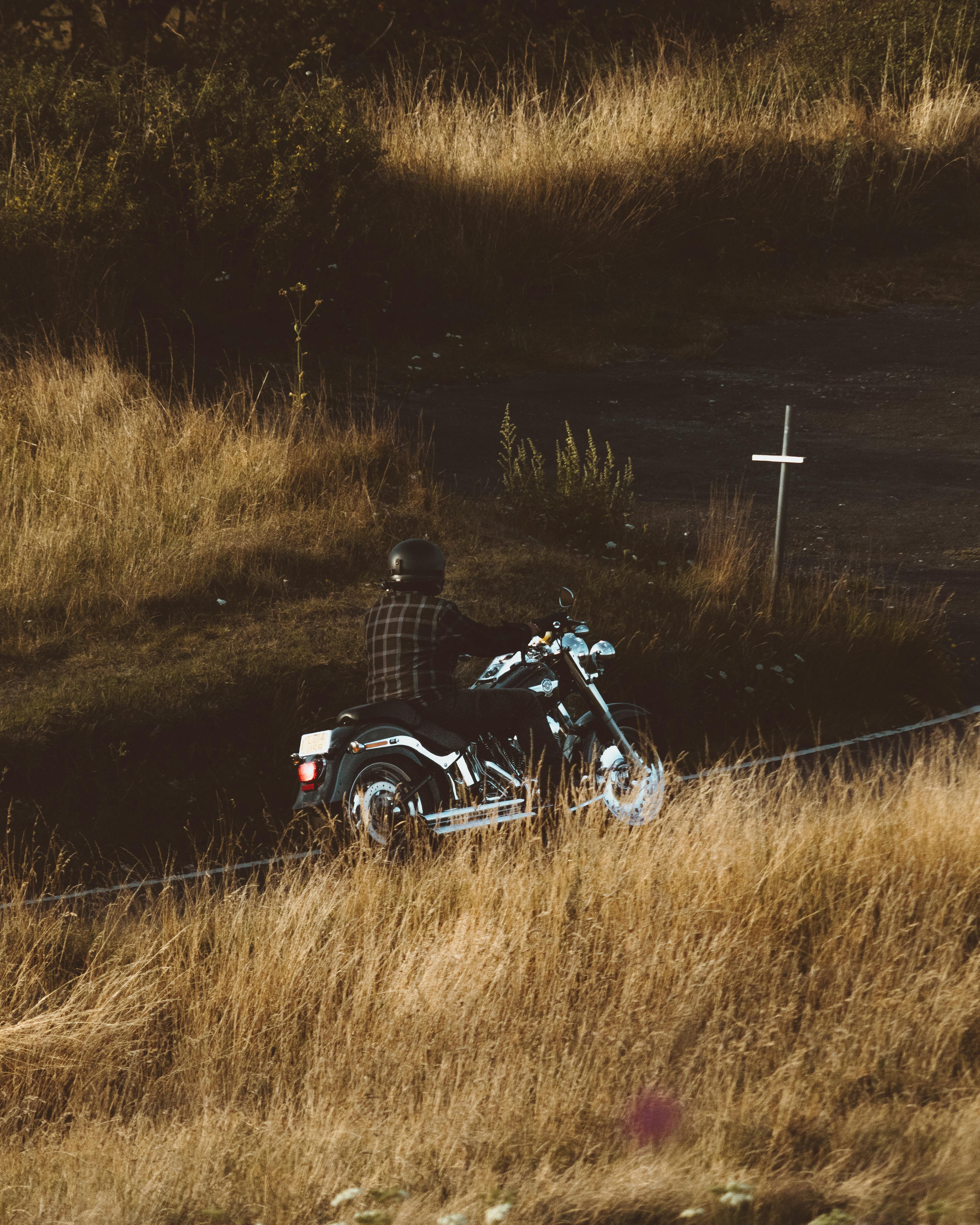 Anonymous male in helmet riding motorbike on road among fields with dry grass in rural terrain in nature in countryside