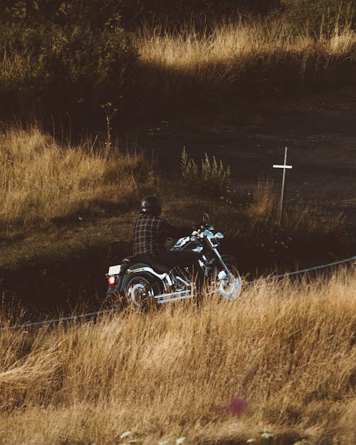 Anonymous male in helmet riding motorbike on road among fields with dry grass in rural terrain in nature in countryside