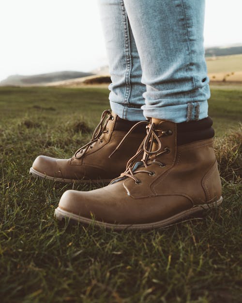 Free Person in Blue Denim Jeans and Brown Leather Boots Standing on a Grass Field  Stock Photo