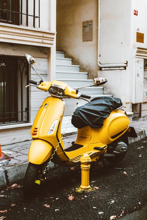 Free Yellow and Black Motor Scooter Parked Beside White Concrete Building Stock Photo