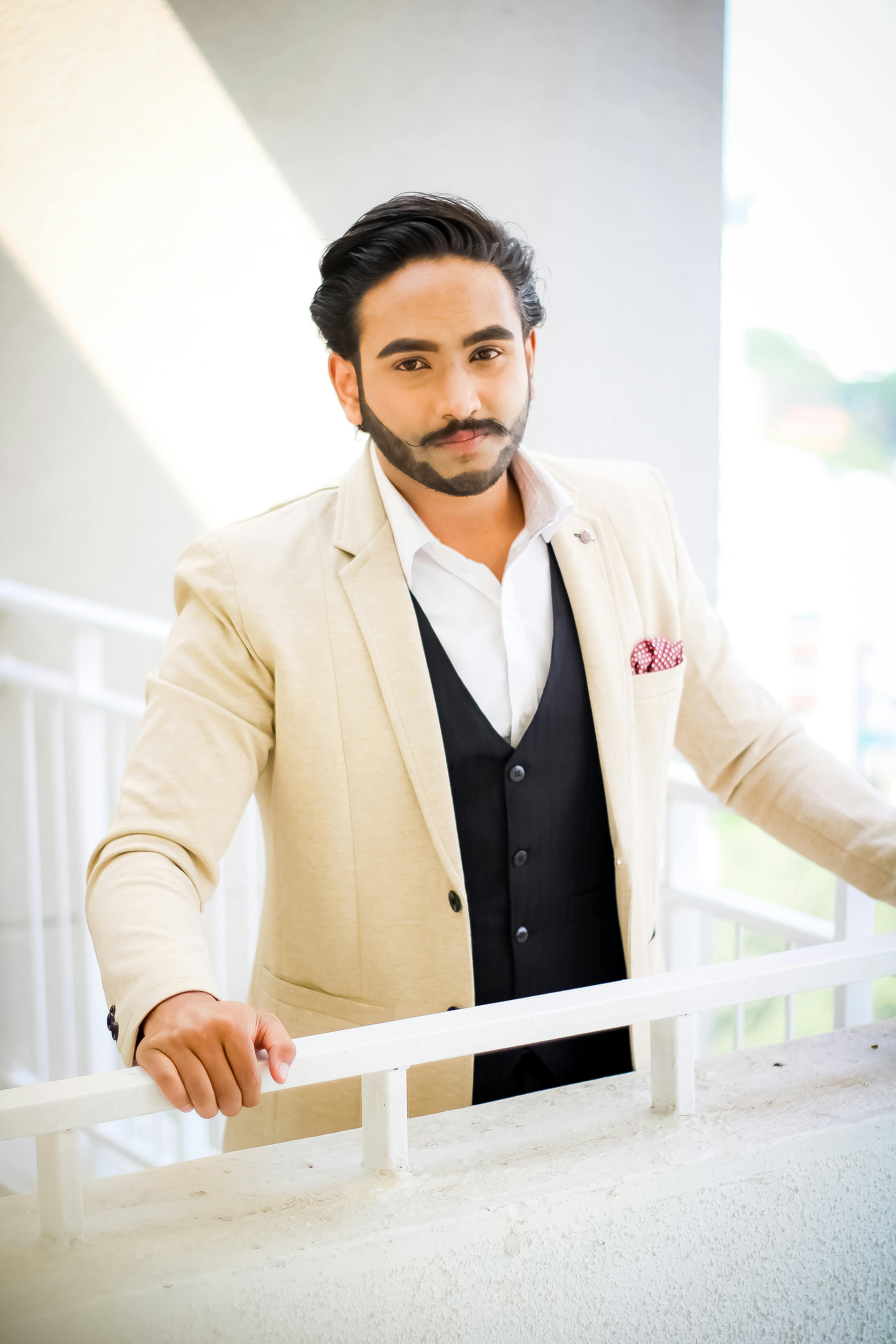 Elegantly dressed man posing confidently outdoors in a beige suit with a black vest, displaying timeless fashion.