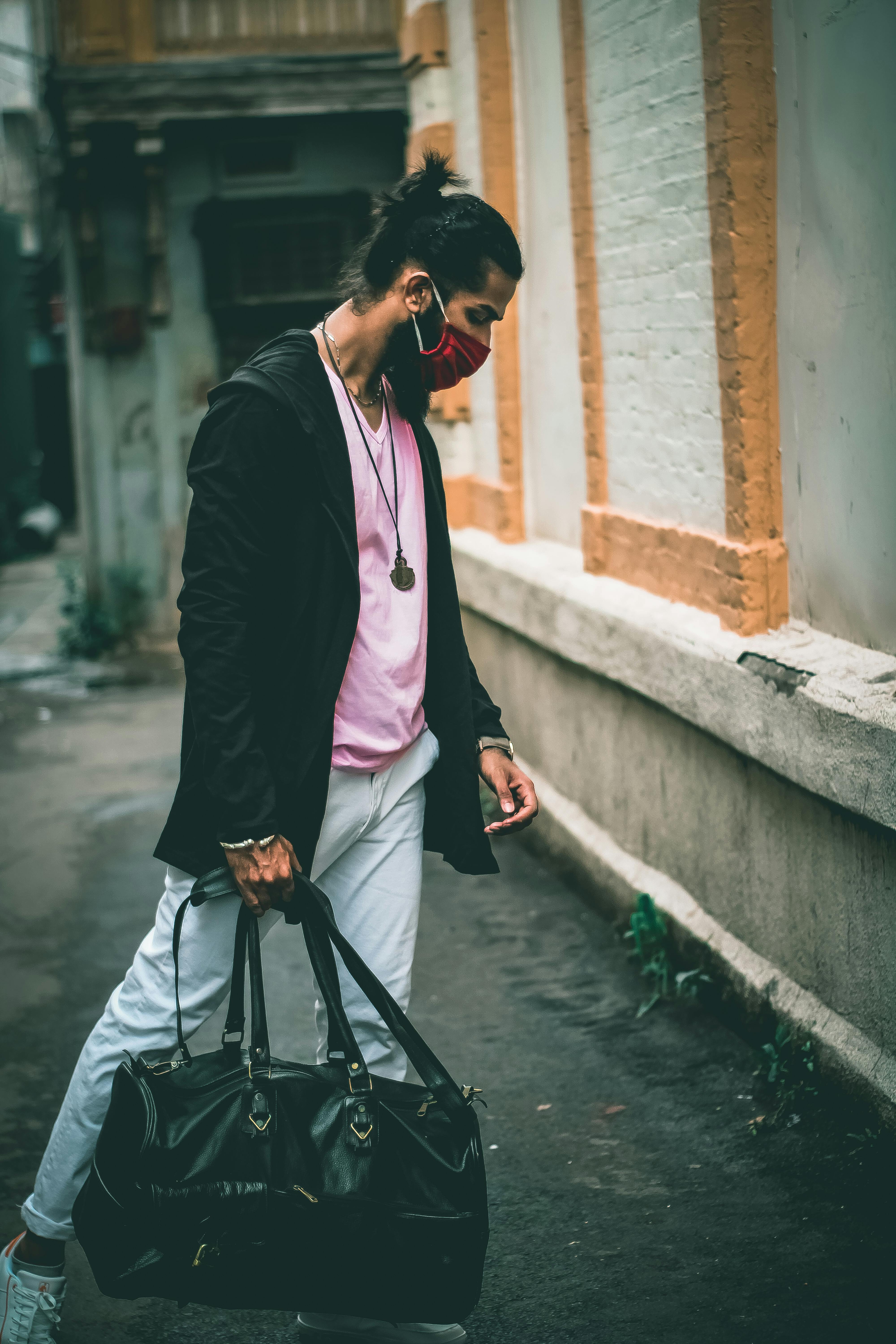 Free Stylish man in jacket and face mask holding duffle bag in urban setting. Stock Photo