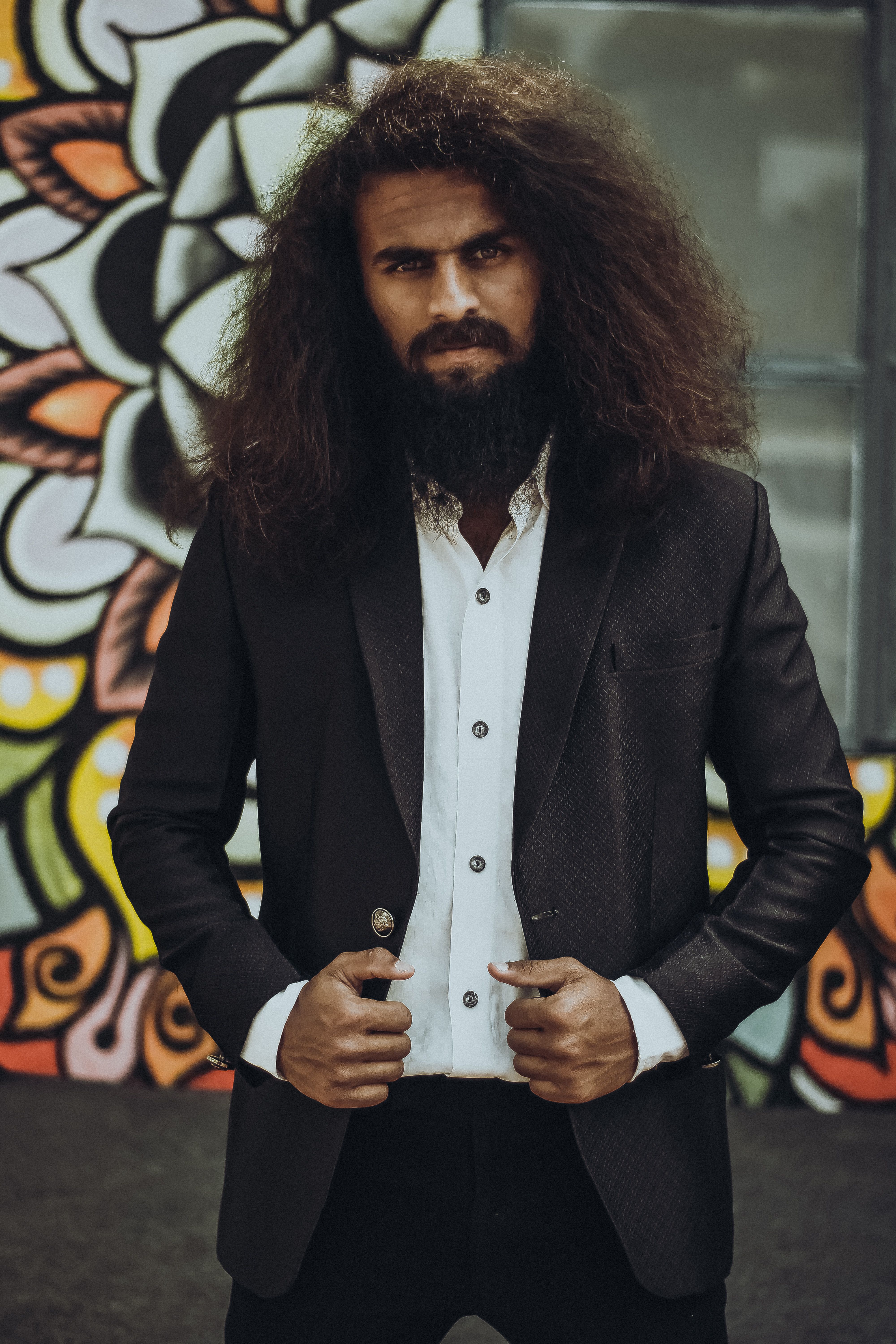 Confident man in elegant suit posing against vibrant urban graffiti wall.