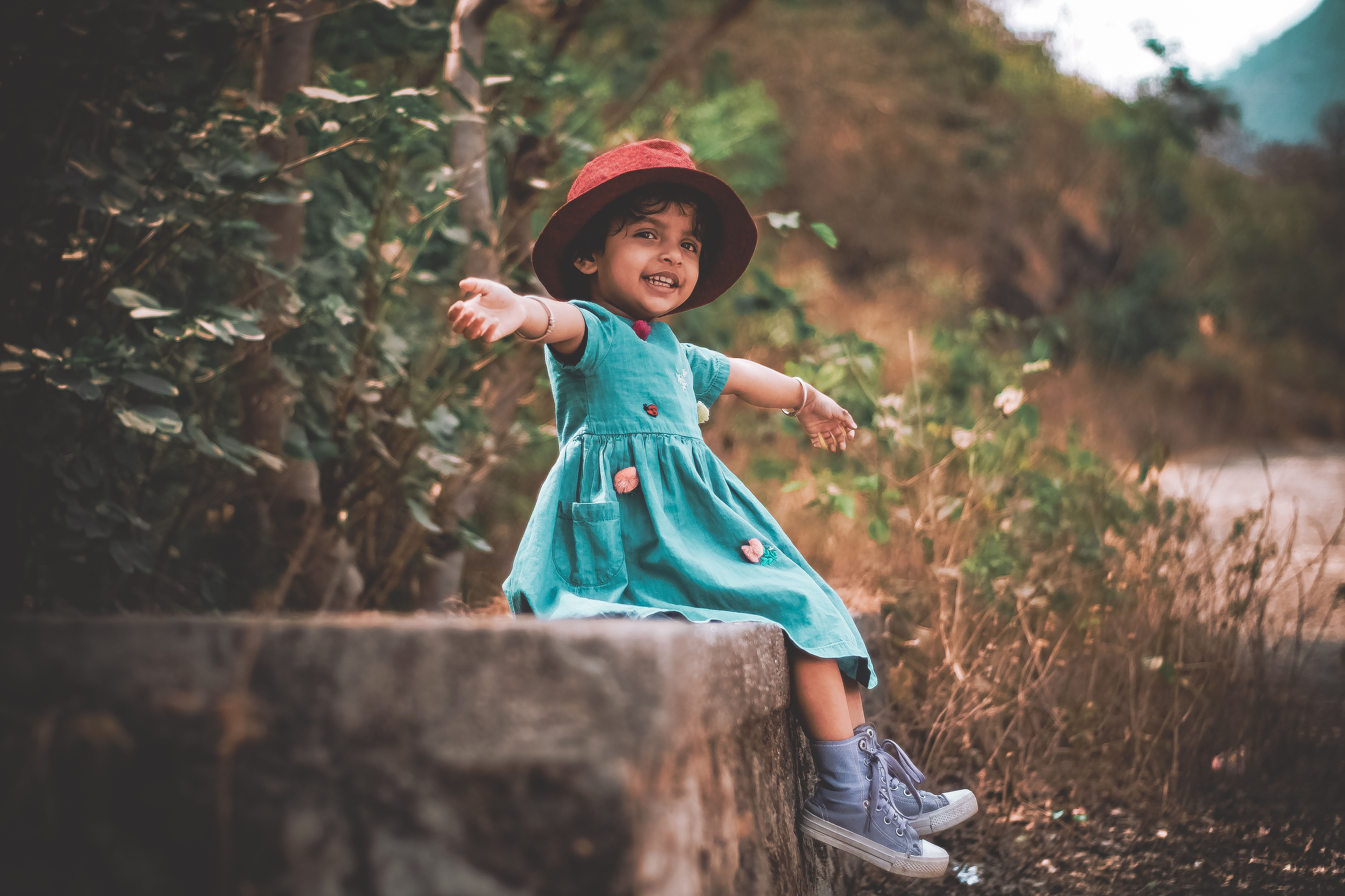 A vibrant young girl in a green dress sits joyfully outdoors, exuding happiness.