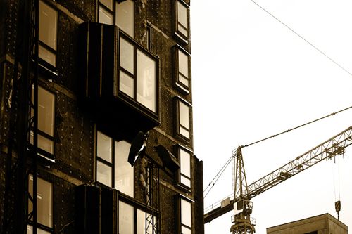 Free Sepia-toned image of a construction site with a building facade and crane. Stock Photo