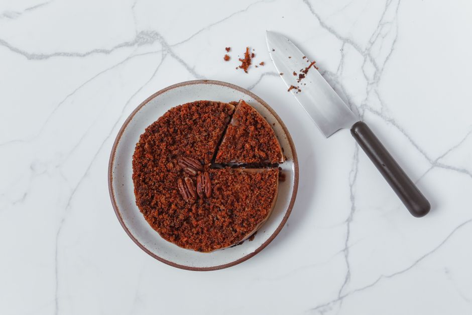 A saucepan of golden coconut pecan frosting being stirred with a spatula, thick and caramel-colored with shredded coconut and chopped pecans folded through it.