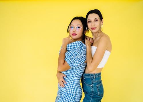 Women Smiling and Standing Beside Yellow Wall