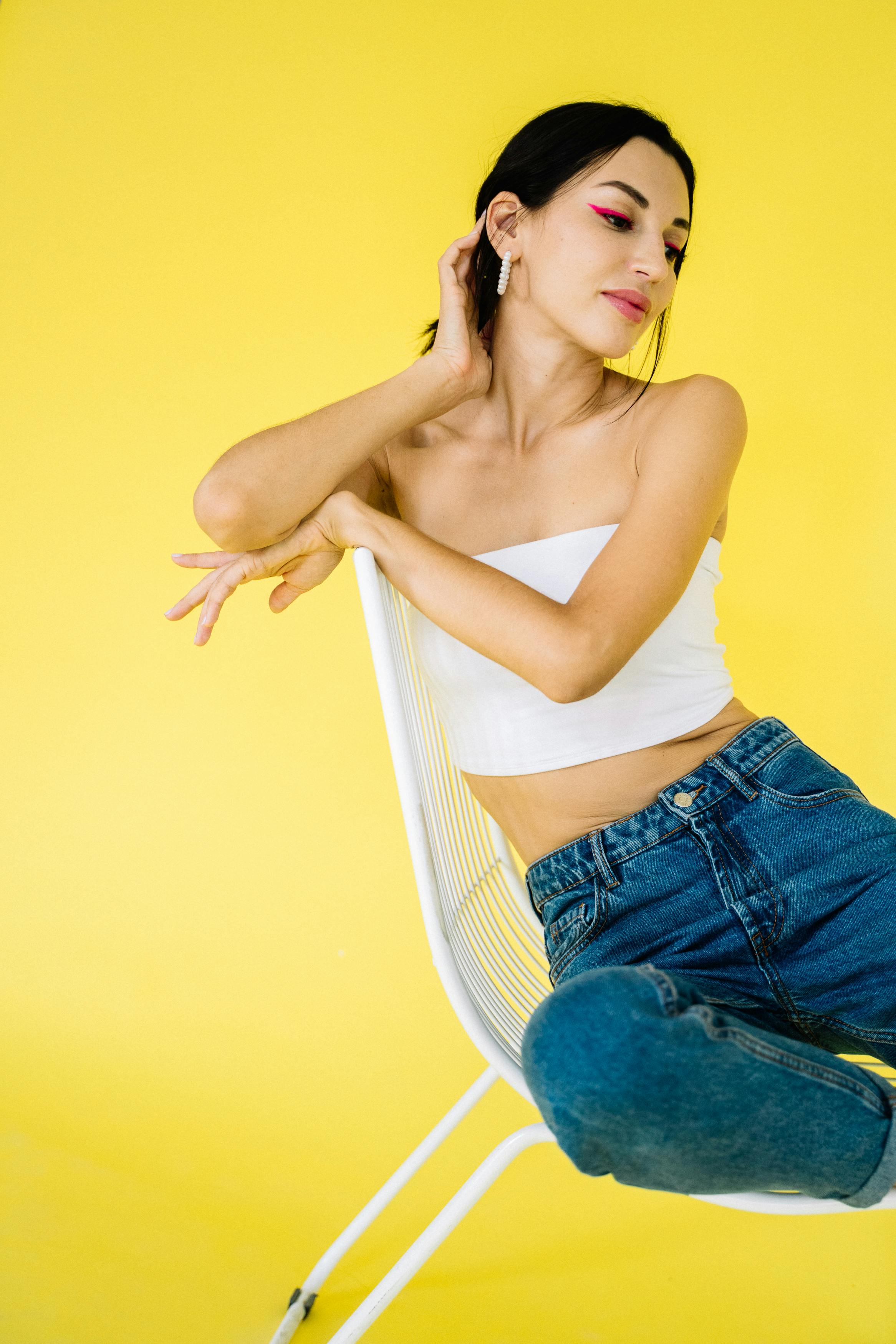 Stylish young woman posing on chair with vibrant yellow backdrop.