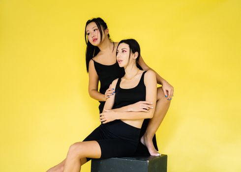 在工作室环境中，两位时尚女性身着黑色连衣裙，在充满活力的黄色背景下摆出姿势
