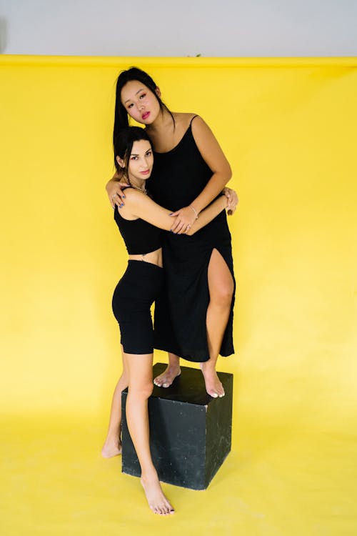 Women in Black Clothes Hugging on Yellow Background