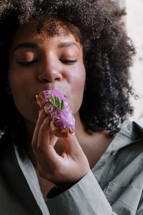 Free Close-up of a woman savoring a delightful purple glazed eclair indoors. Stock Photo