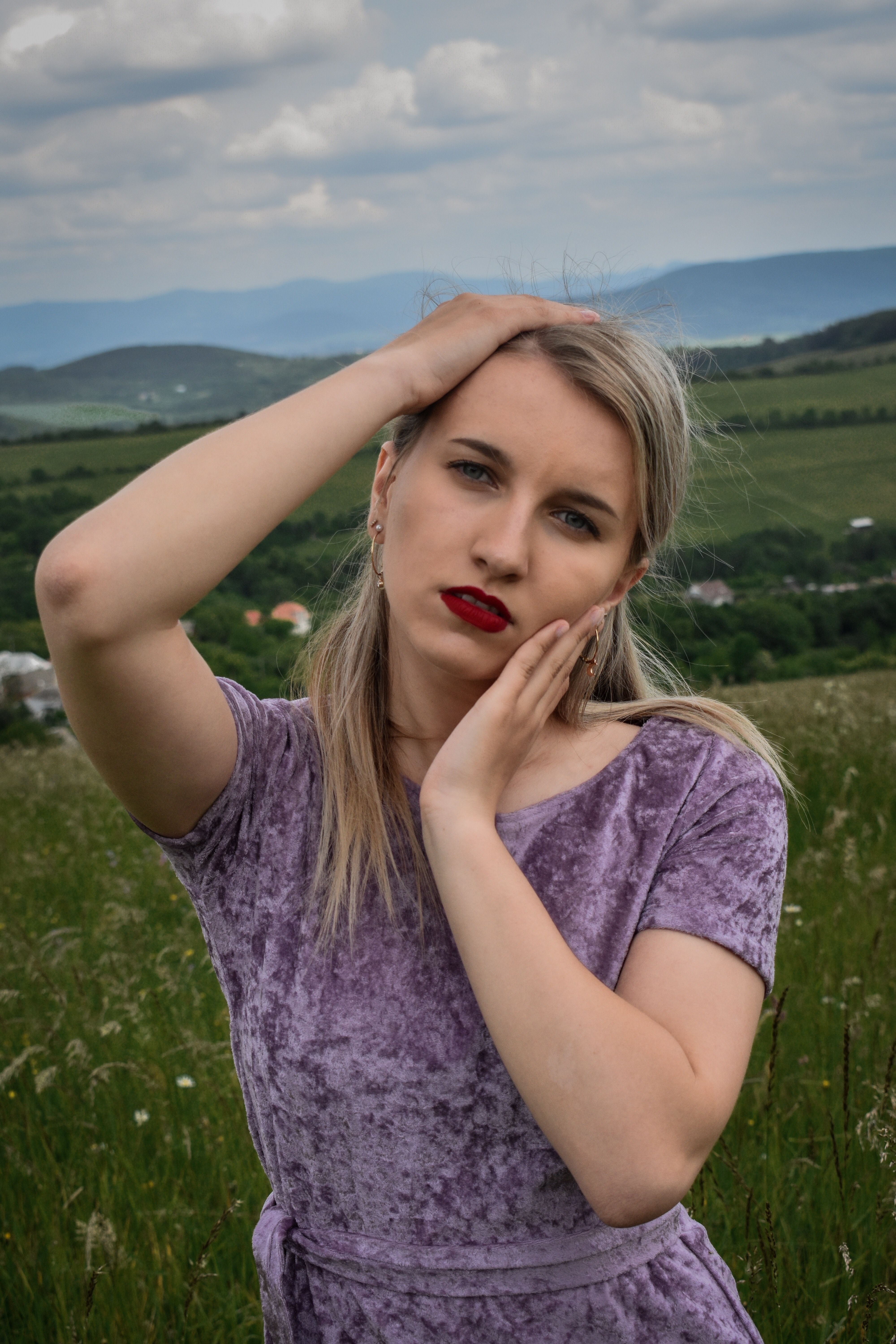 Elegant fashion portrait of a woman posing in the countryside with a purple dress.