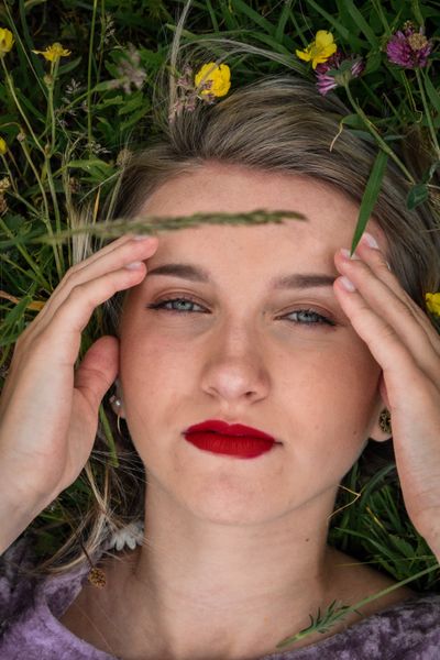 Close-up of a woman lying in grass with hands framing her face