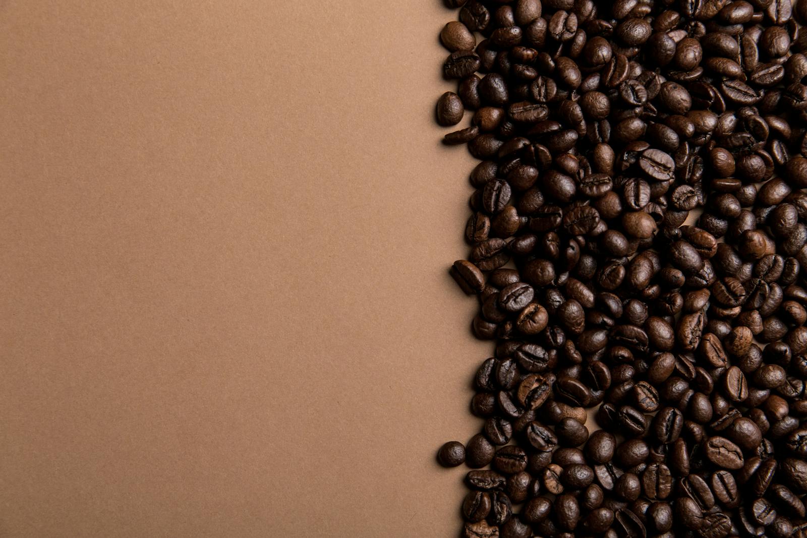 Roasted coffee beans scattered on a brown surface with copy space