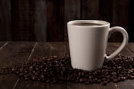 木桌上放着一个质朴的陶瓷杯，杯里盛满了热咖啡，周围散落着咖啡豆