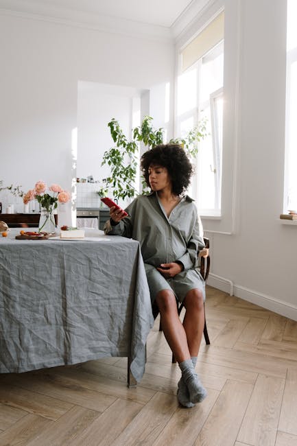 Expectant mother in home setting, relaxing with phone by table during the day.
