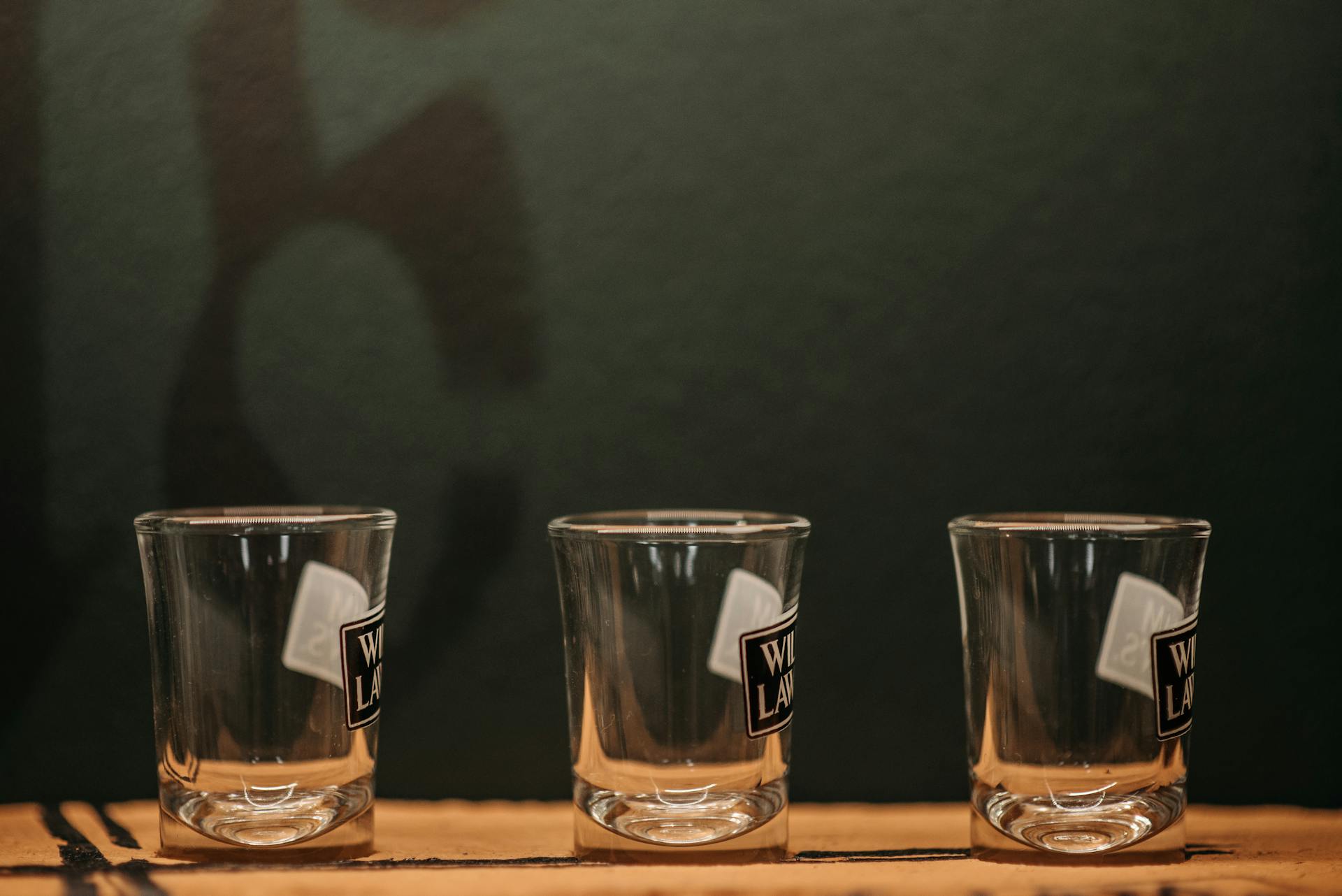 Three empty shot glasses aligned on a wooden table, ideal for bar or party themes.