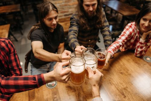 Free Friends enjoying a cheerful toast with beer mugs at a cozy bar setting. Stock Photo