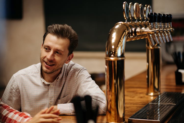 A Man In Checkered Long Sleeves Standing At The Bar