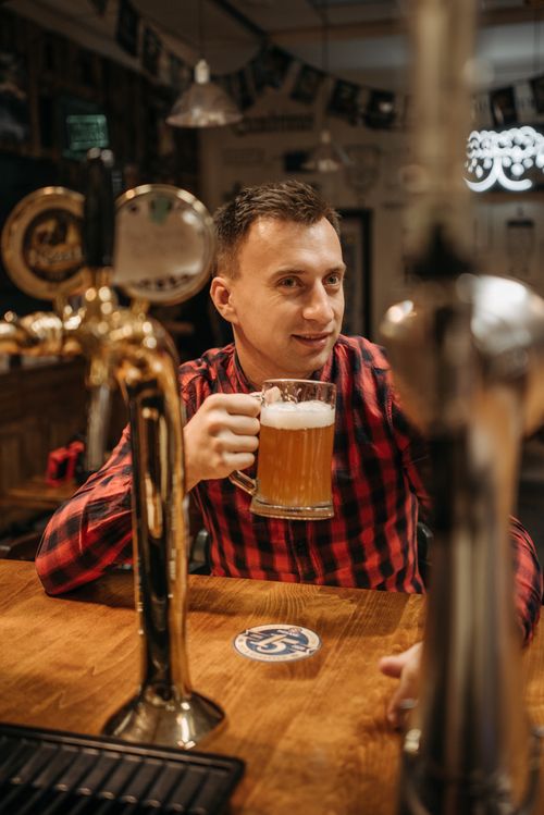 Free Man in a plaid shirt enjoys a draft beer in a cozy bar setting. Stock Photo