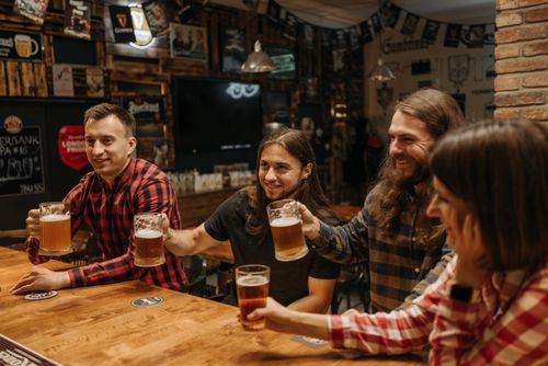 Free Group of friends clinking glasses and enjoying beer at a lively bar setting. Stock Photo