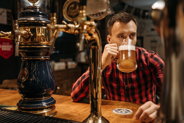 A Man In Plaid Long Sleeves Drinking Beer