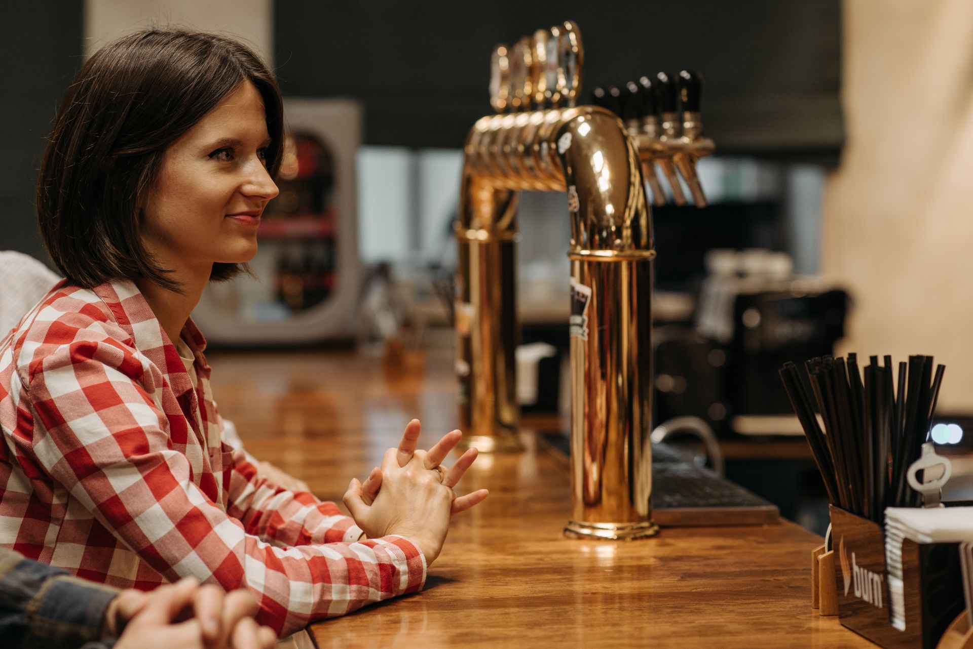 Woman seated at a rustic bar counter with brass beer taps in the background.