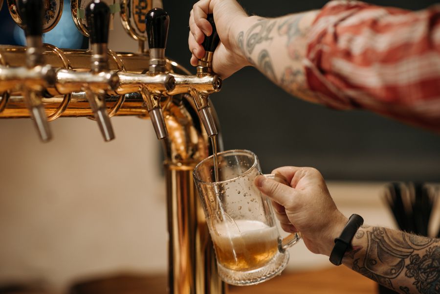 A bartender pulling a glass of craft beer from brass taps